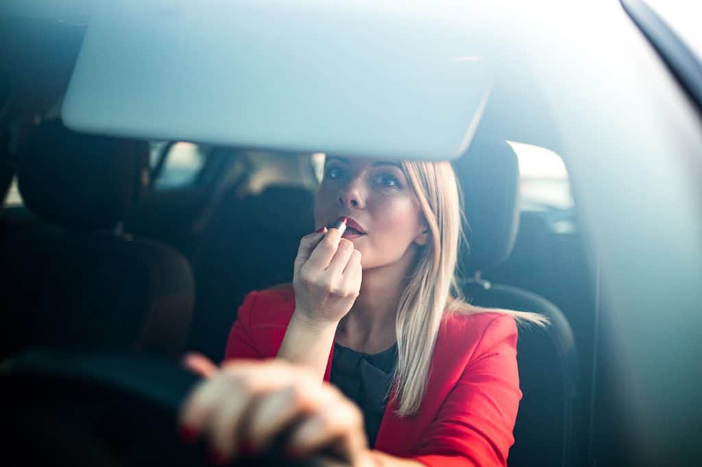 A blonde woman applying lipstick while driving